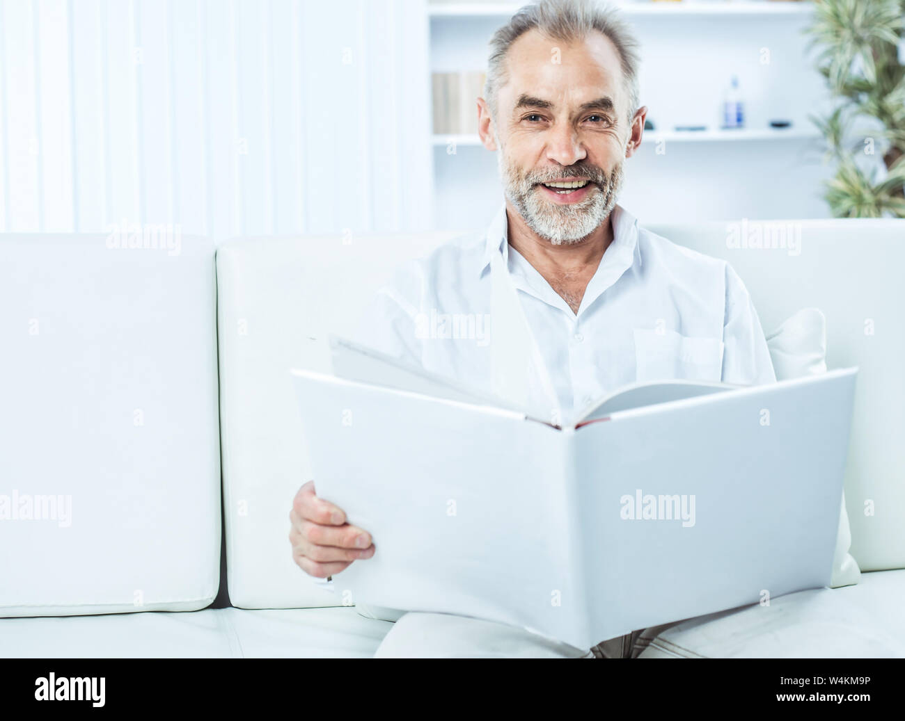 businessman with a magazine sitting on sofa in bright office. the photo has a empty space for your text Stock Photo