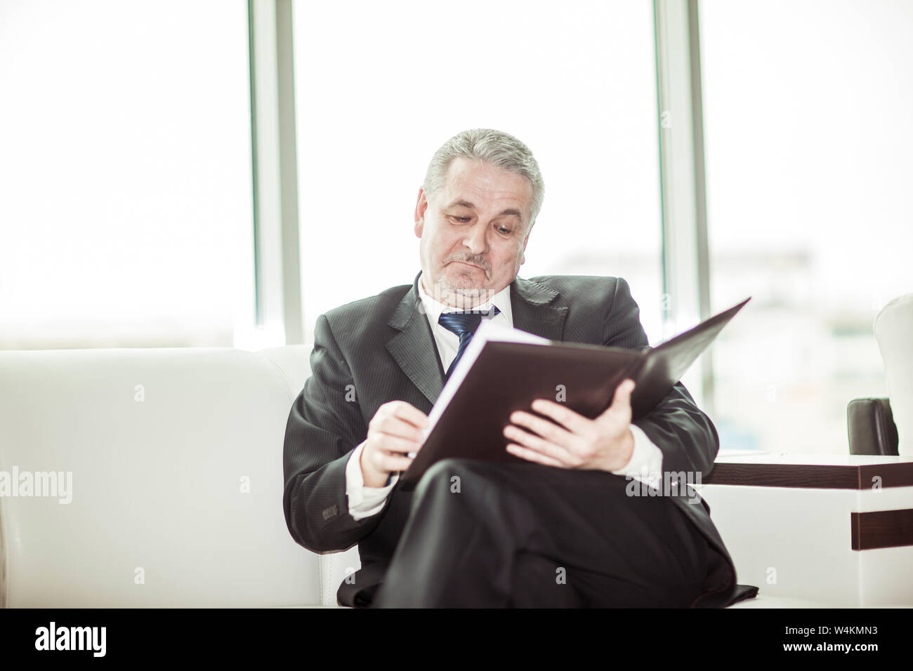 experienced lawyer reviews the documents with the terms of a new contract sitting on the sofa in the private office. Stock Photo