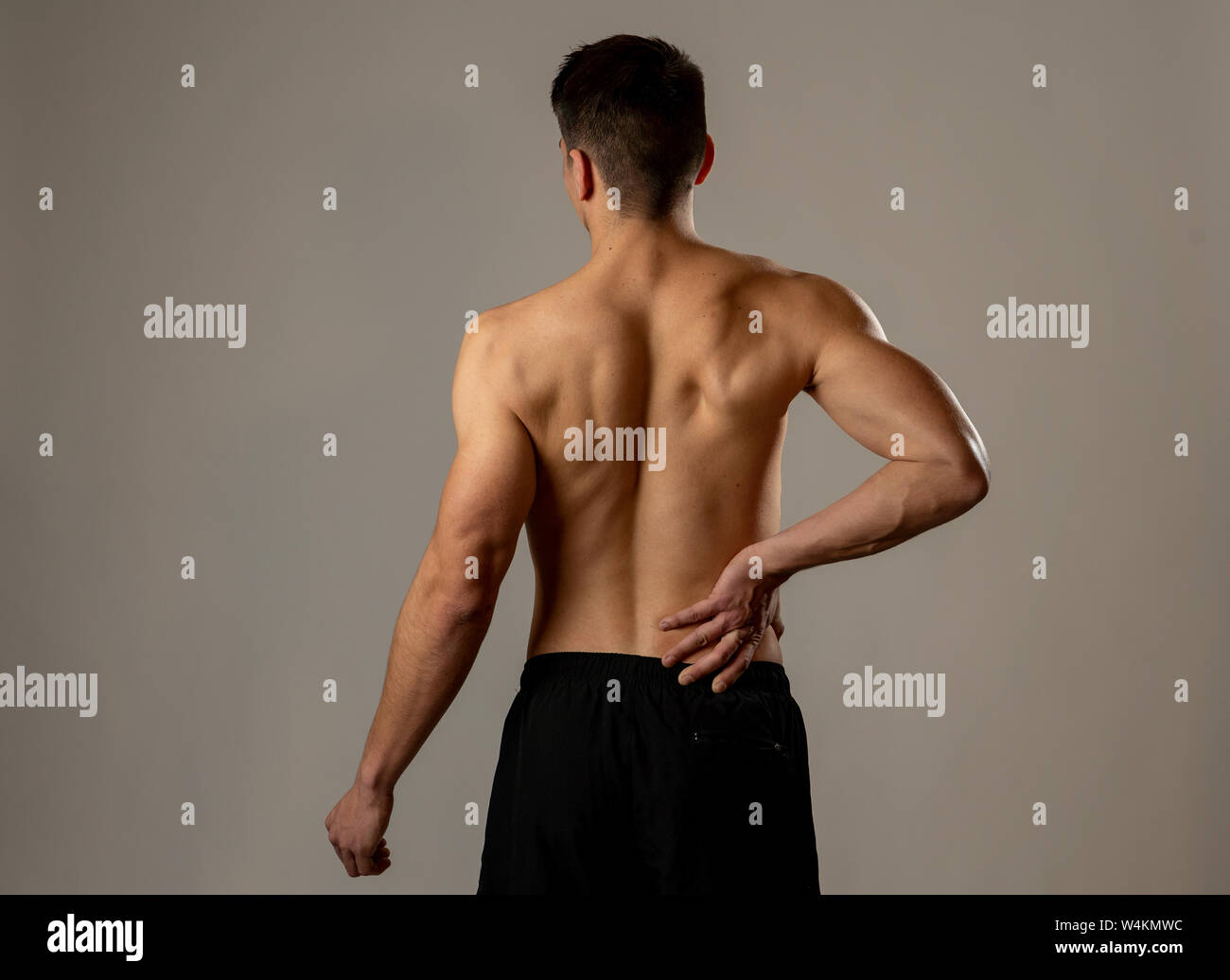 Young muscular fitness man touching and grabbing his lower back suffering strong pain after workout. Isolated on neutral background. In sport injury I Stock Photo Alamy