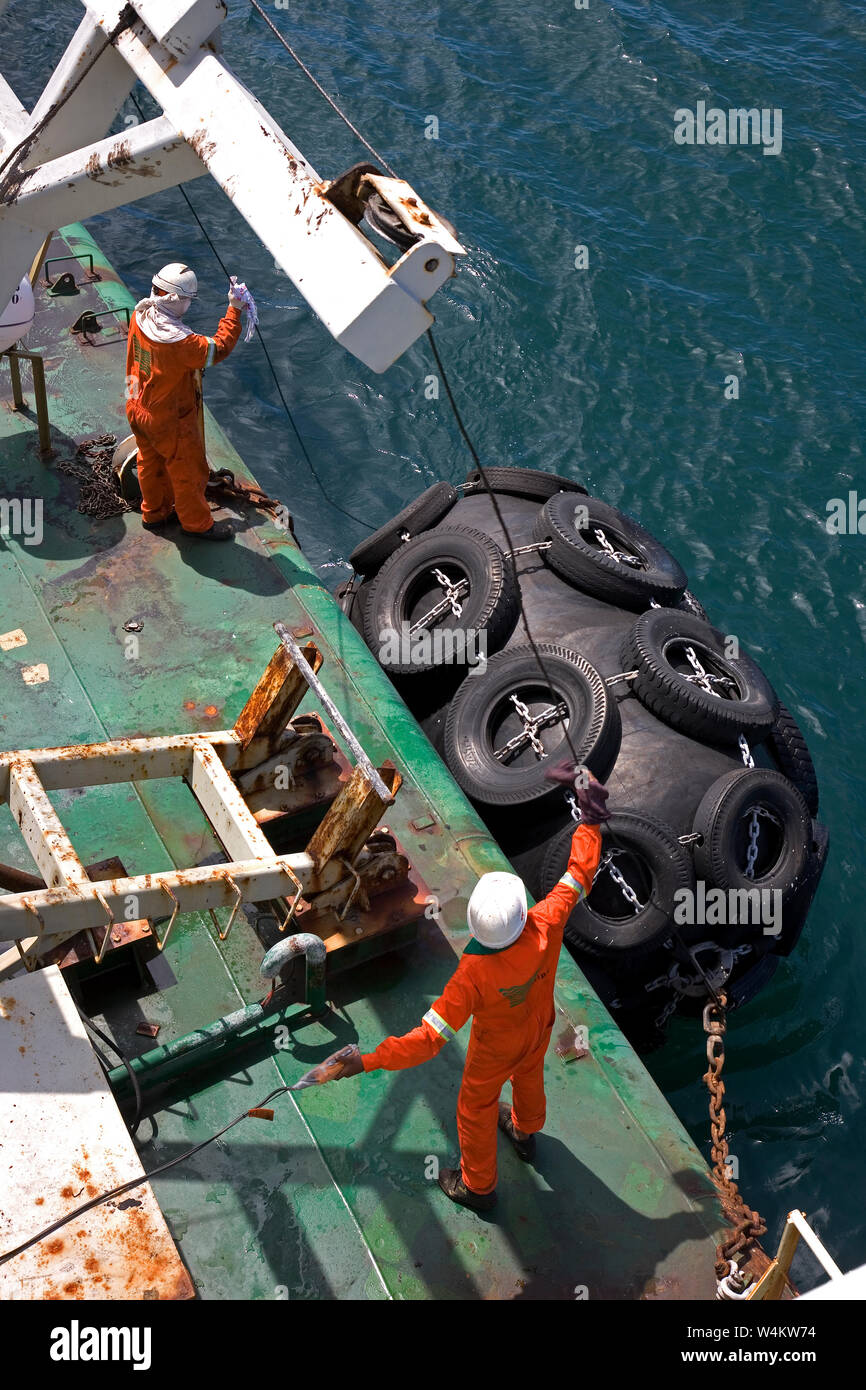 Mining, managing & transporting of titanium mineral sands. Barge crew lowering mooring buoys ready to go alongside bulk carrier to discharge cargo. Stock Photo