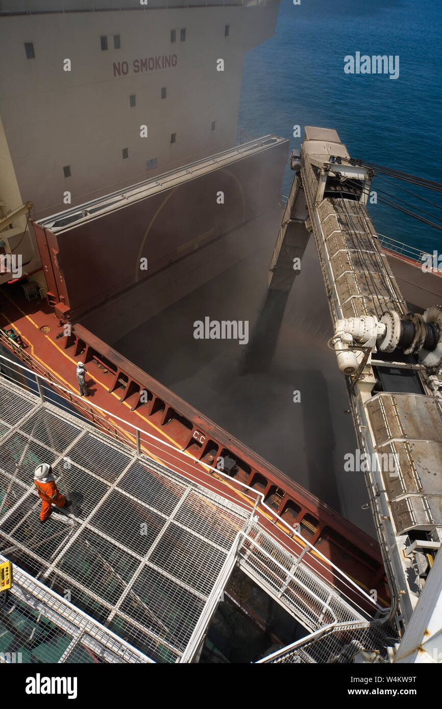 Mining, managing & transporting of titanium mineral sands. Loading mineral sands cargo via transhipment barge boom into hold of bulk carrier at sea. Stock Photo