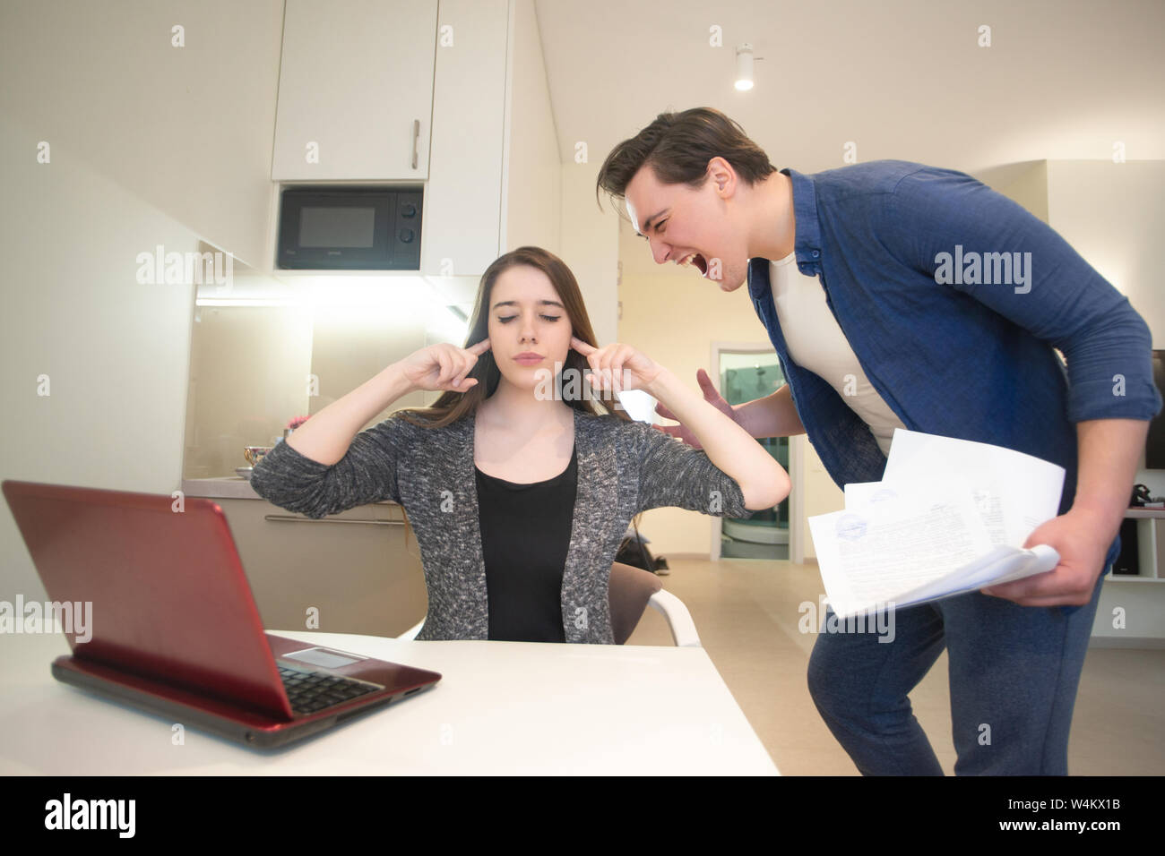 quarrelling couple young handsome man shouting on beautiful woman covering her ears having unpleasant conversation in the dinning room Stock Photo
