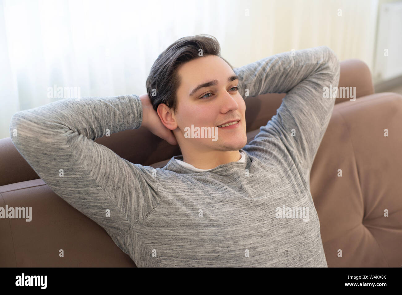 young handsome man sitting on the sofa with his hands behind head feeling relaxed and cozy Stock Photo