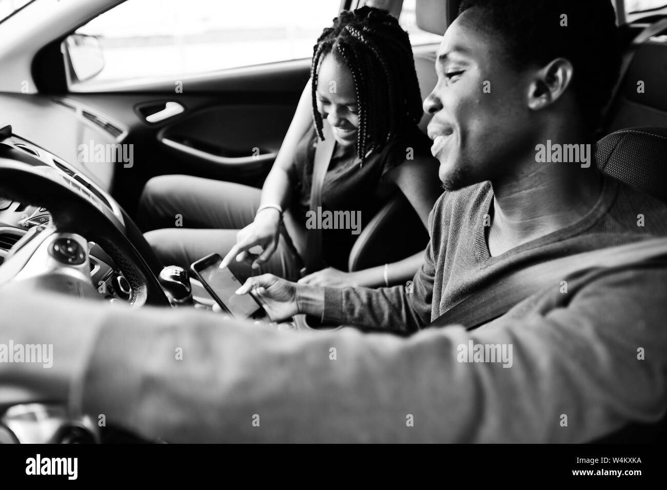 Beautiful young african american couple sitting on the front passenger seats while handsome man driving a car. Looking at map on phone. Stock Photo