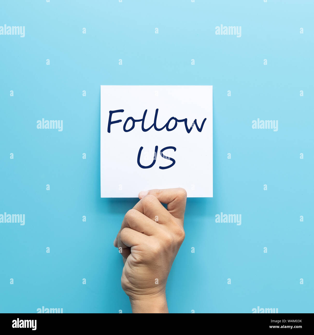 hand holding white paper with text follow us isolated on blue background. social media trend and internet marketing concept Stock Photo