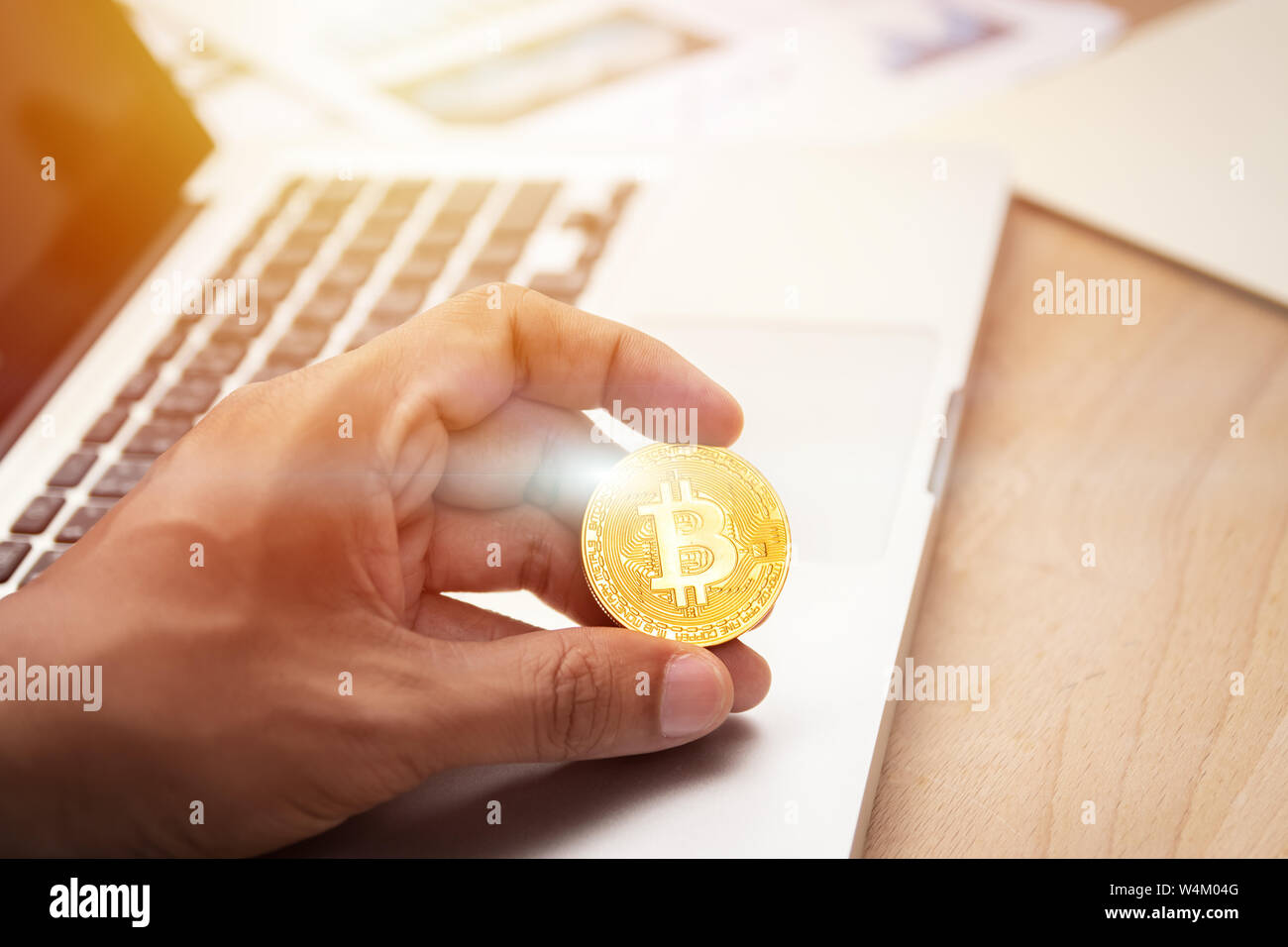 businessman holding cryptocurrency golden bitcoin coin in hand with computer laptop at background. crypto currency, electronic virtual money for web b Stock Photo