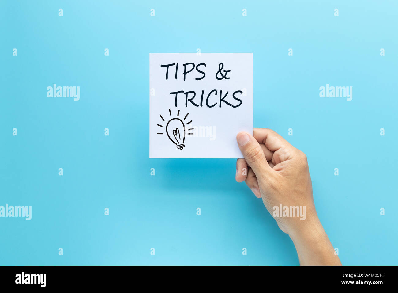 text tips and tricks on white paper in hand isolated on blue background Stock Photo