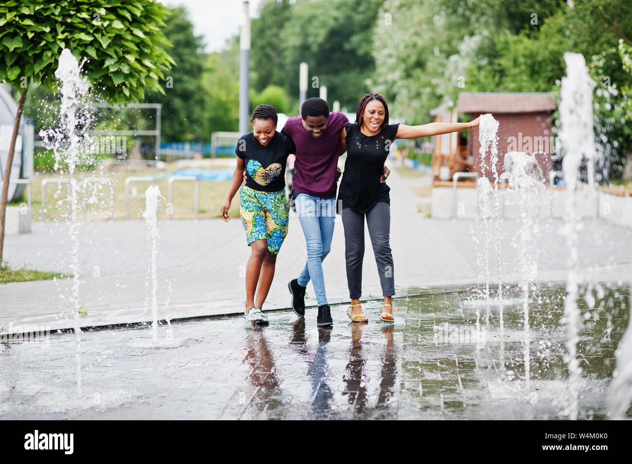 Three african american friends walking on fountains. Having fun ...