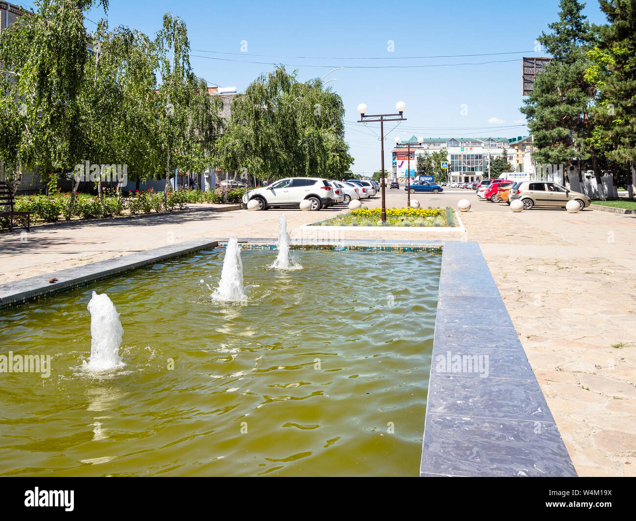ABINSK, RUSSIA - JULY 2, 2019: water fountain and car parking on Komsomolskaya street in Abinsk city in summer. Abinsk is town and administrative cent Stock Photo