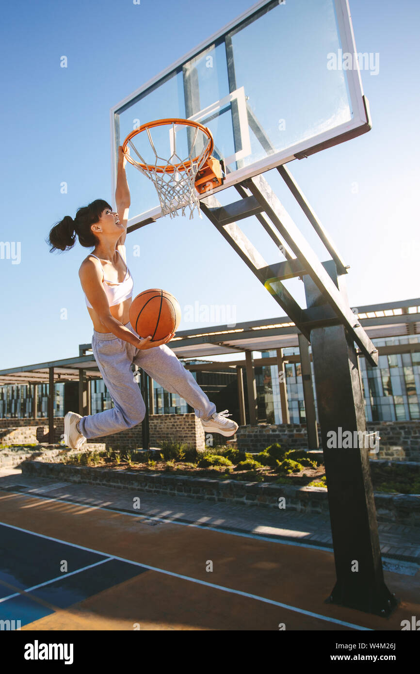 Female playing basketball outdoors on summer day. Woman basketball player making slam dunk. Stock Photo