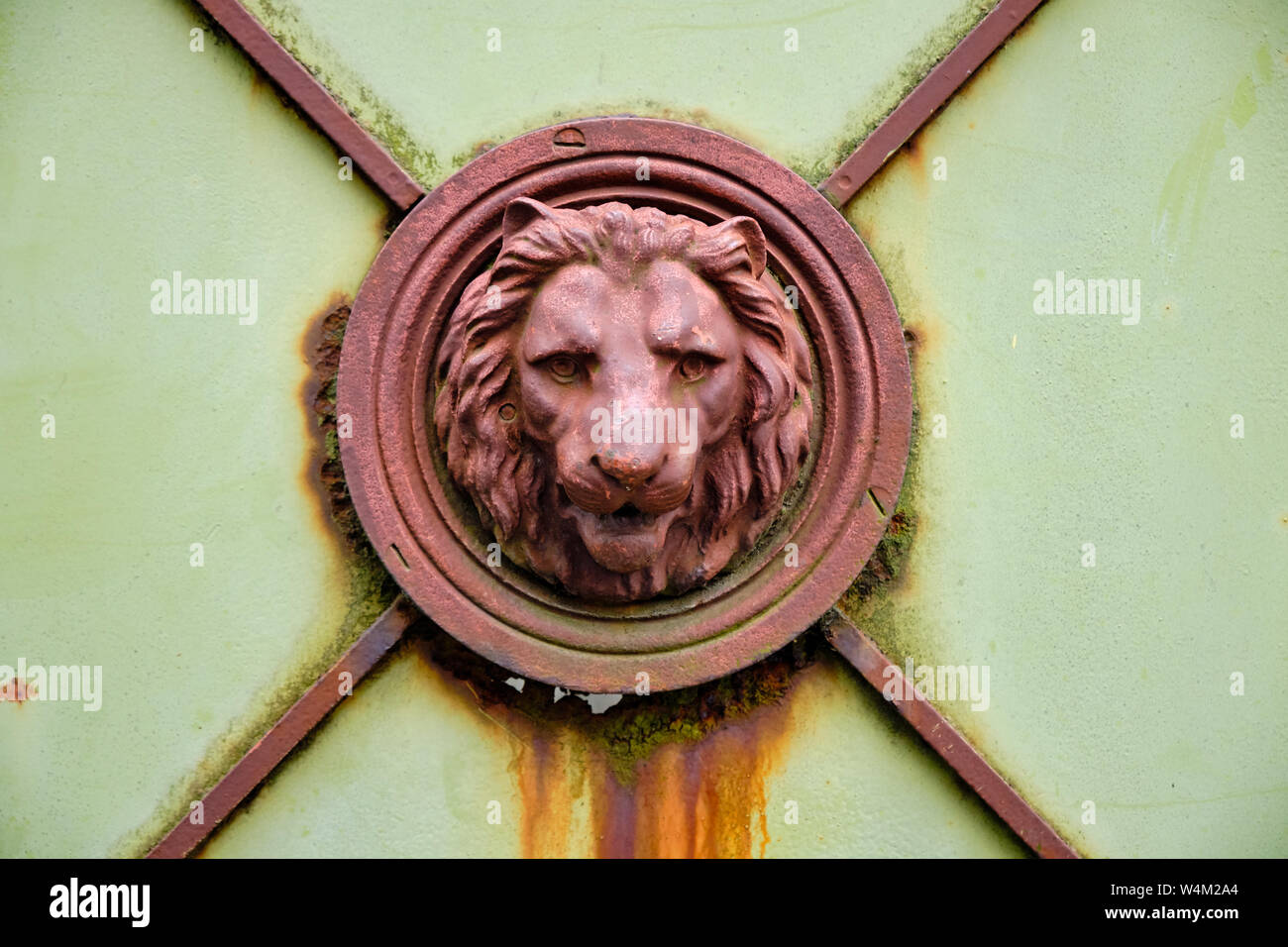 Rusted metal Lion head framed in concentric circles on close up of old rusted green metal door Stock Photo