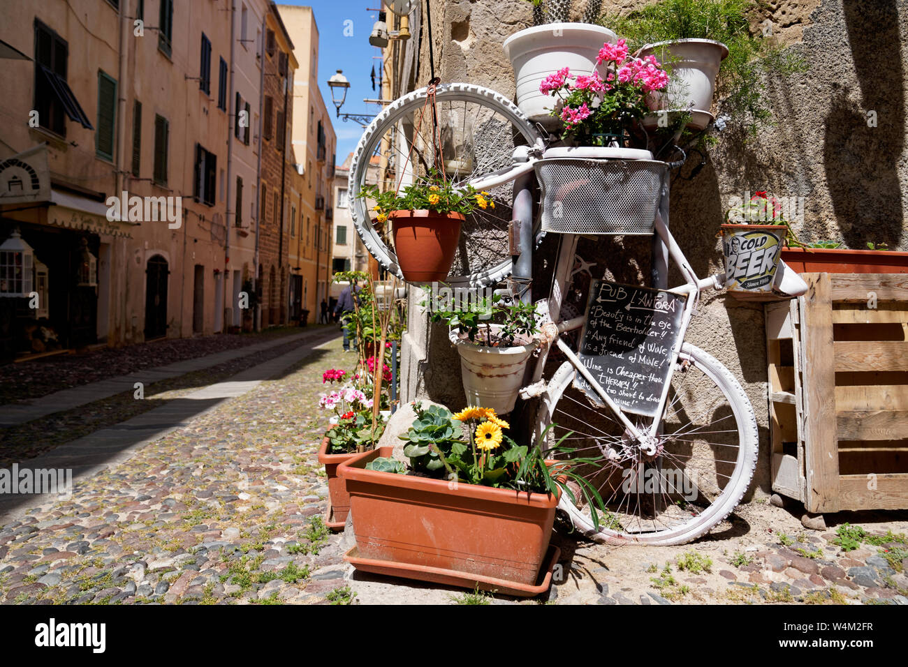 Picturesque flower decoration of a bicycle with wine quote on a chalkboard at a street corner in Alghero (Sardinia) Stock Photo