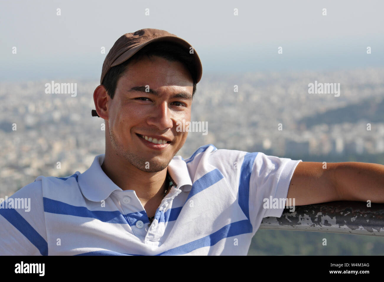 Handsome and smiling young man wearing a baseball cap sitting in the sun Stock Photo