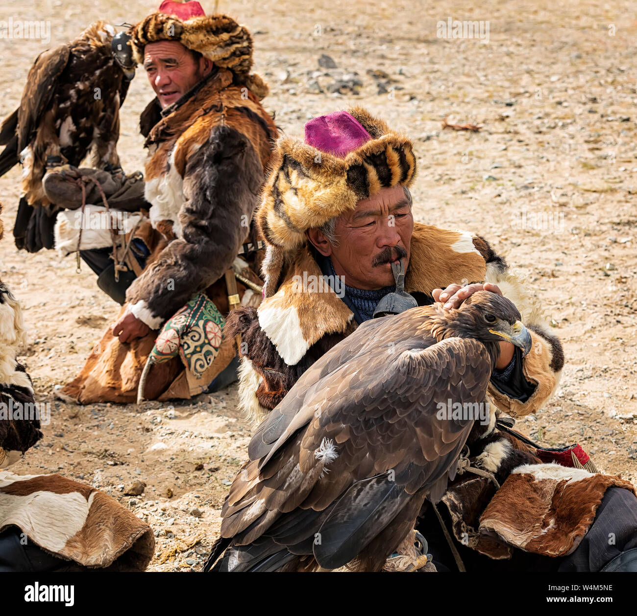 Altai eagle festival. Hunters are  sitting with their  Golden Eagles on the Hand. Close up. Main focus on  man which  is in the foreground Stock Photo