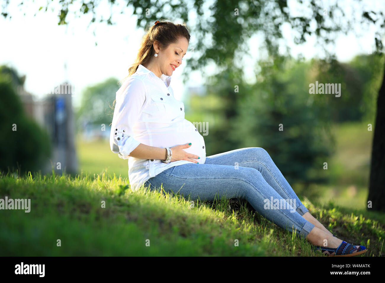 pregnant woman sitting on the grass in a Park on a Sunny day Stock Photo