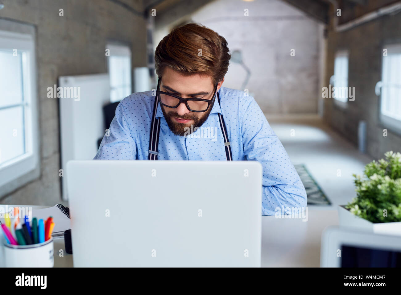 Handsome hipster working on his laptop in modern, industrial office Stock Photo