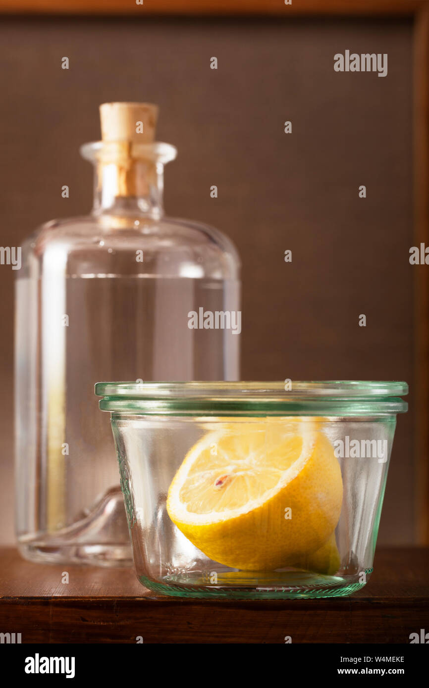 Half a lemon in a vintage small glass pot and a bottle of water on a wooden table Stock Photo
