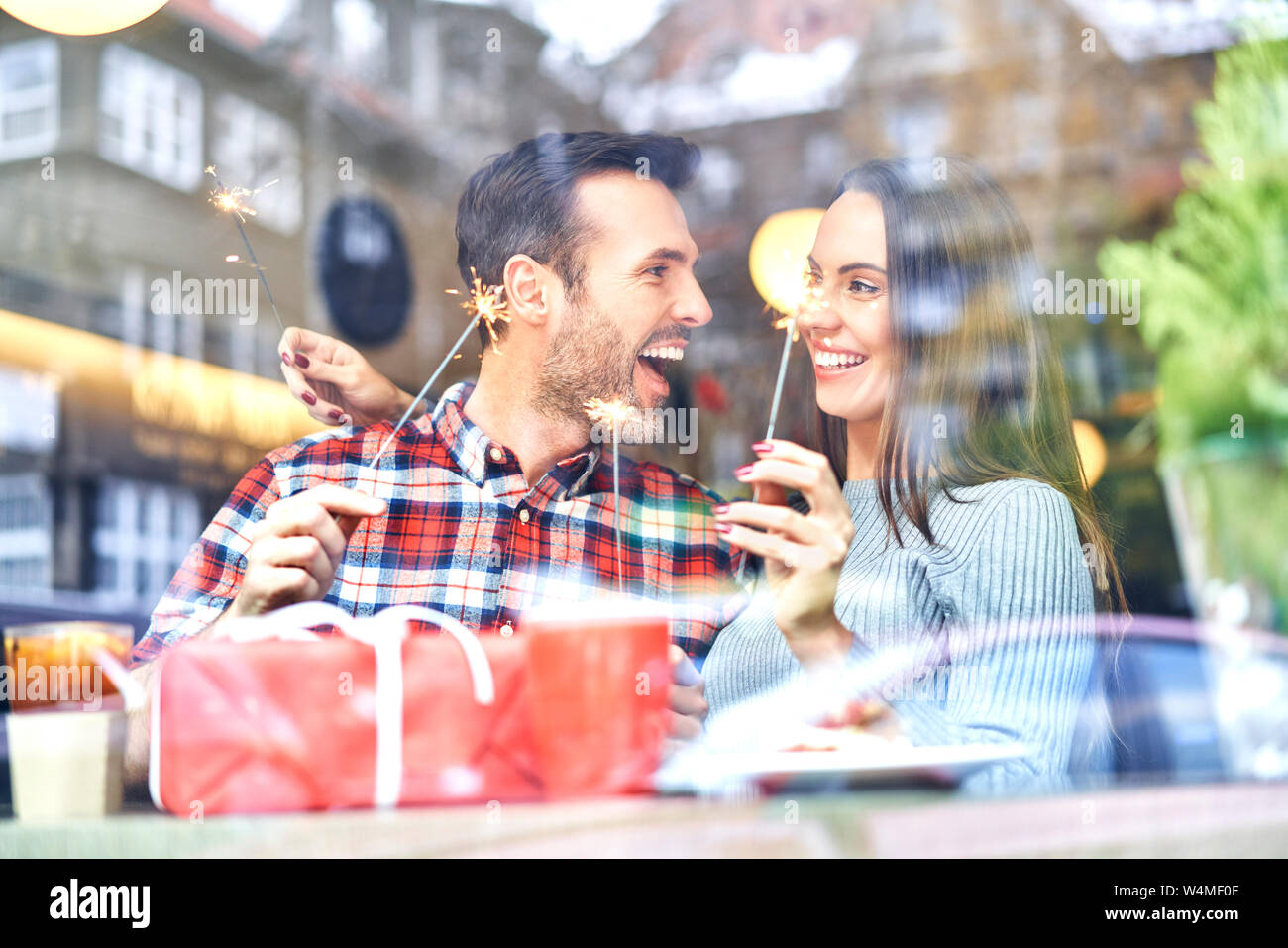 Couple playing with sparklers while sitting with present in cafe during Christmas time Stock Photo