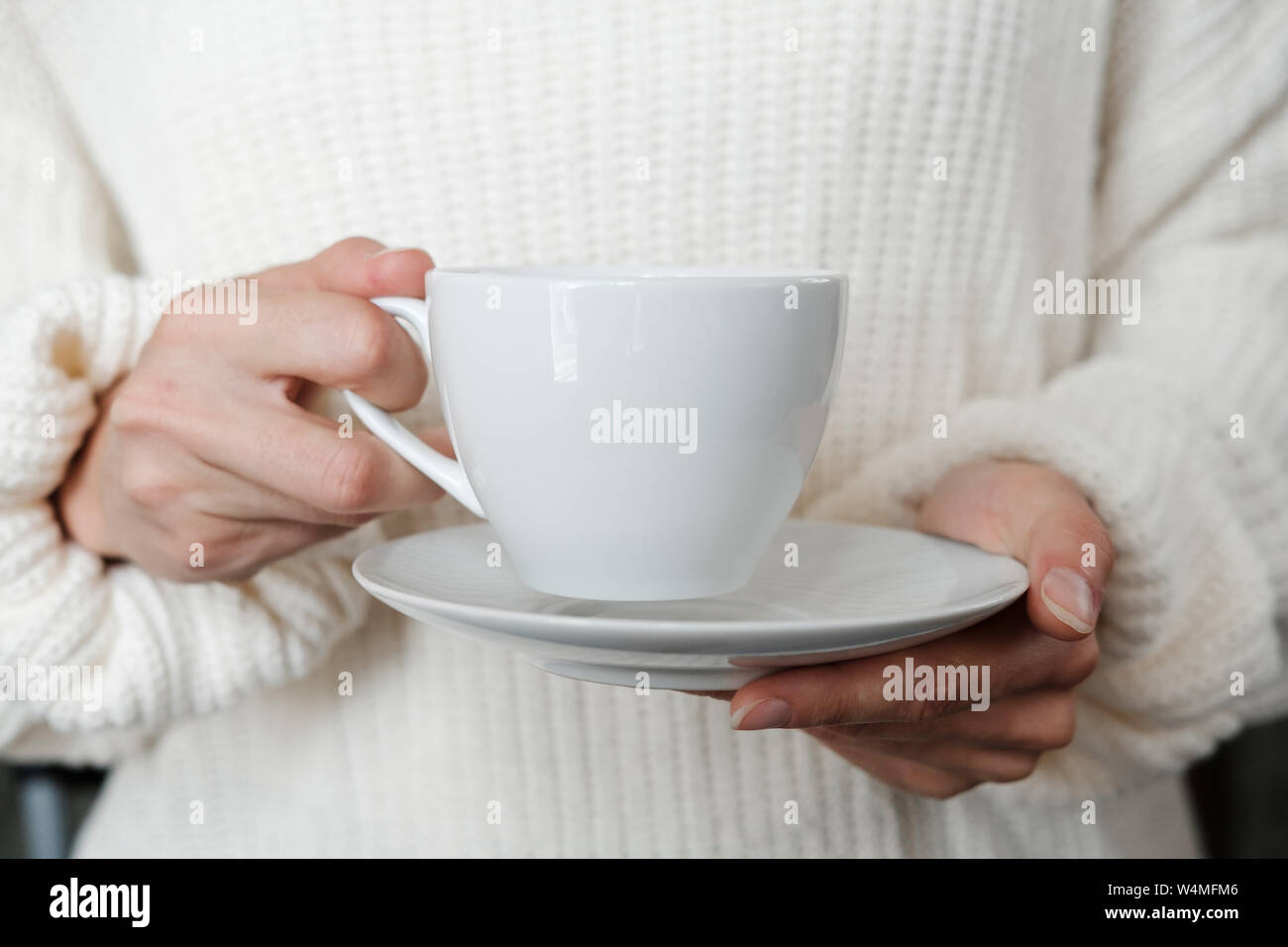 Woman in white knitted sweater holding cup of coffee. Female hands with cup of tea. Close up Stock Photo