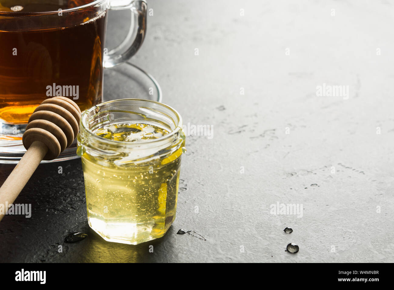 Flower light organic honey in glass jar with tea with wooden stick on dark background with copy space. Folk remedy against flu in rainy season. Autumn Stock Photo