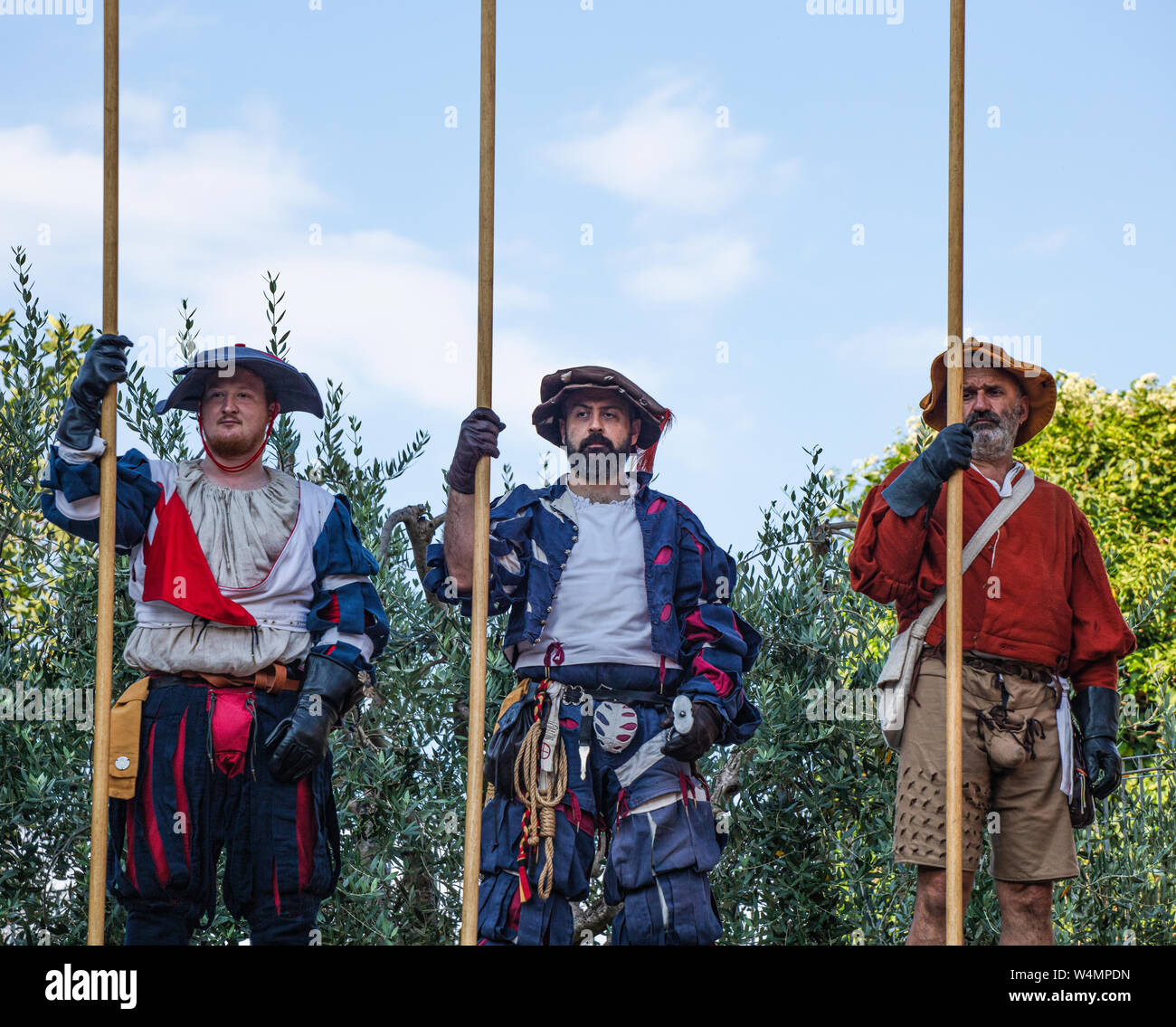 Three local actors in Renaissance costume and carrying lances waiting to take part in the summer festival in a small town in Italy. Stock Photo
