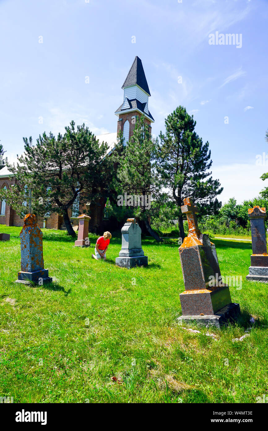 Abandon Country Grave Yard with old church with old tumestones and  woman praying and paying respect to her assisters on her knees in worship. Stock Photo