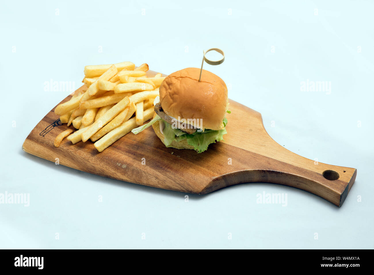 A low contrast Hero Shot of a grilled chicken slider burger, fries on a wooden platter board, on a minimal white background with a 45 degree angle fro Stock Photo