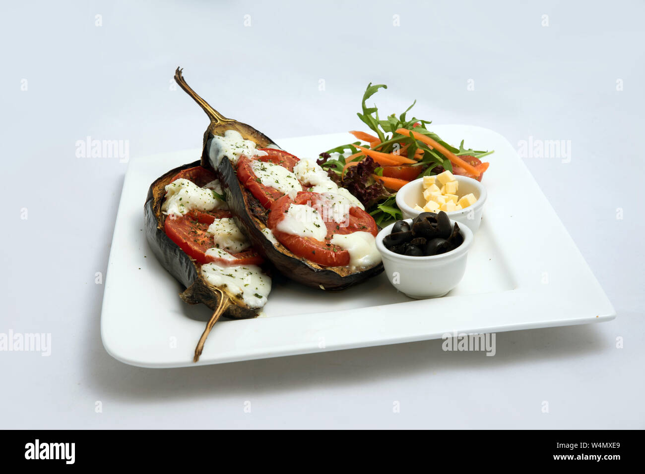 A low contrast warm Hero shot of a main course platter with grilled aubergine with buffalo cheese, tomato, olives & vegetables on the side, on a minim Stock Photo
