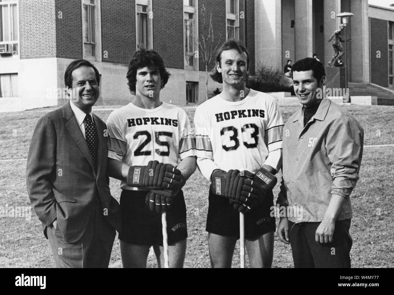 A portrait of President Steven Muller (far left) and Johns Hopkins University lacrosse coach Henry Ciccarone (far right) pose with two Hopkins lacrosse players in uniform wearing their gloves and holding their lacrosse sticks on campus at Johns Hopkins University, Baltimore, Maryland, 1976. From the Historical Photographs Collection. () Stock Photo