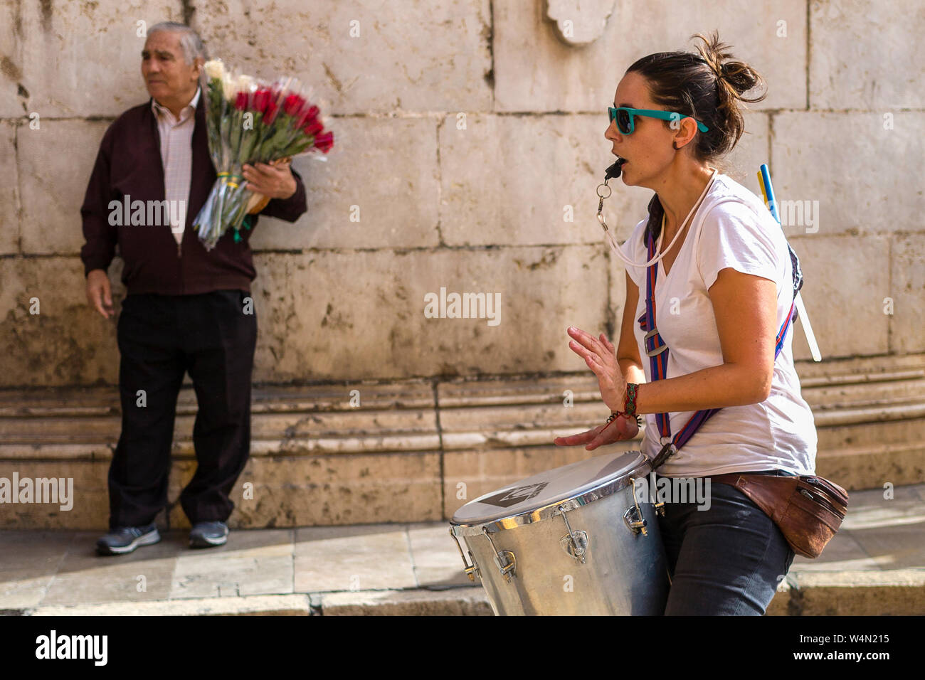 Woman drummer protesting in march with older man flower seller in background, Malaga, Spain Stock Photo