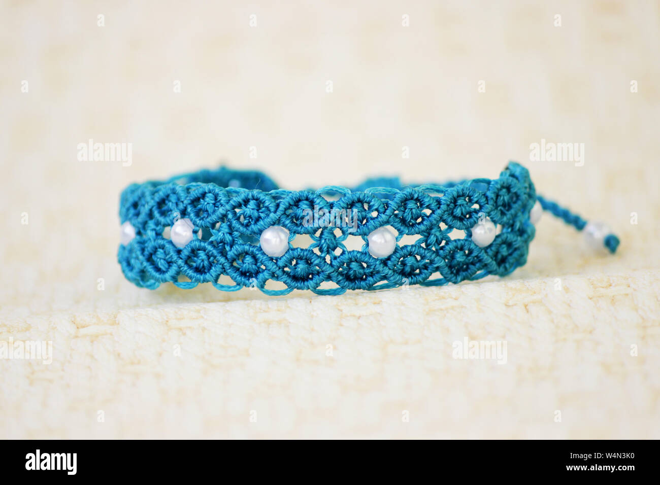 turquoise bracelete with white beads for the hand from waxed thread in the technique of macrame. Handmade Stock Photo