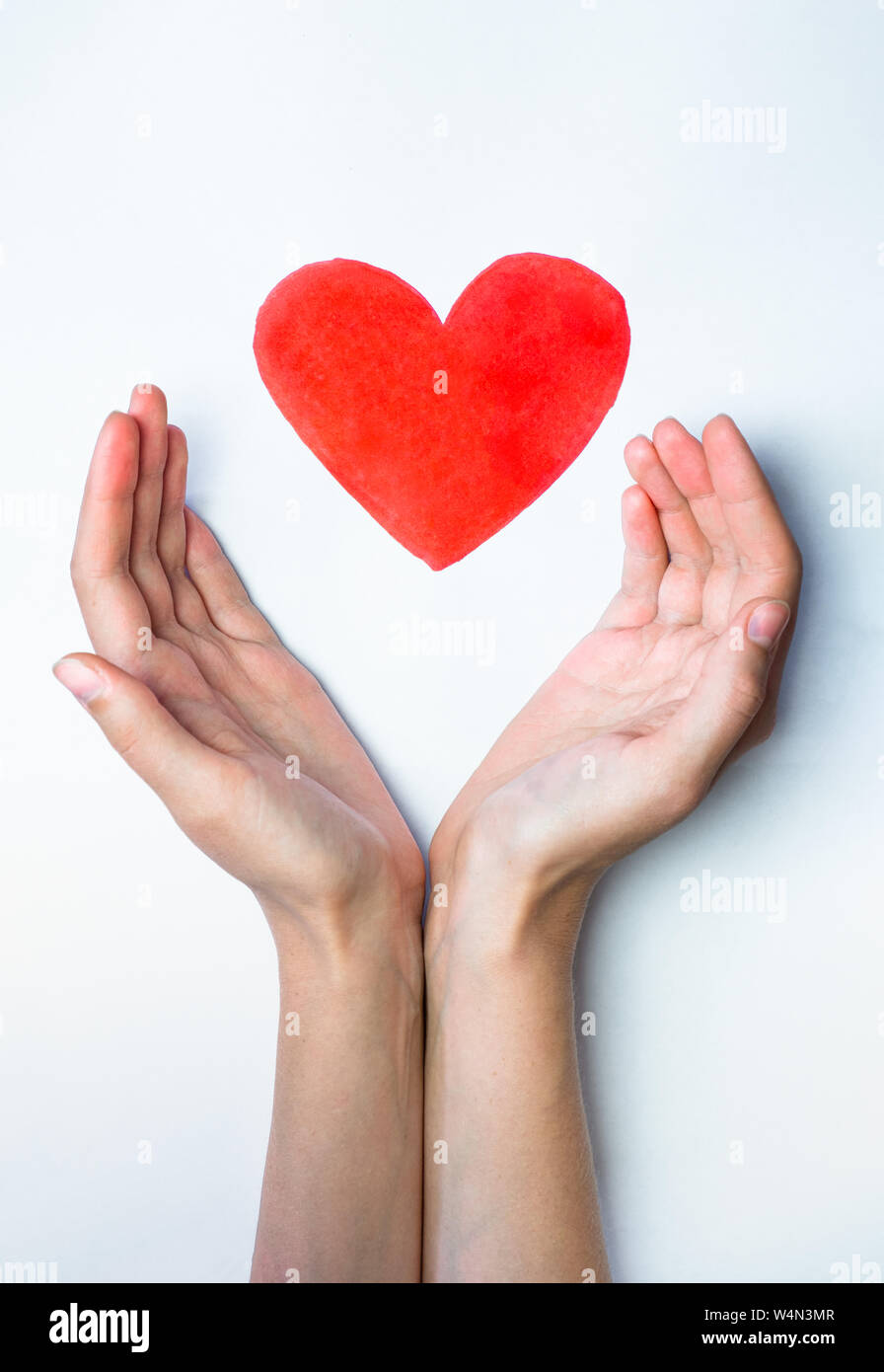 Heart sign drawn with a marker pen and hands embracing it. Concept of love, care and peace: shape of a heart resting safely in human palms. Stock Photo