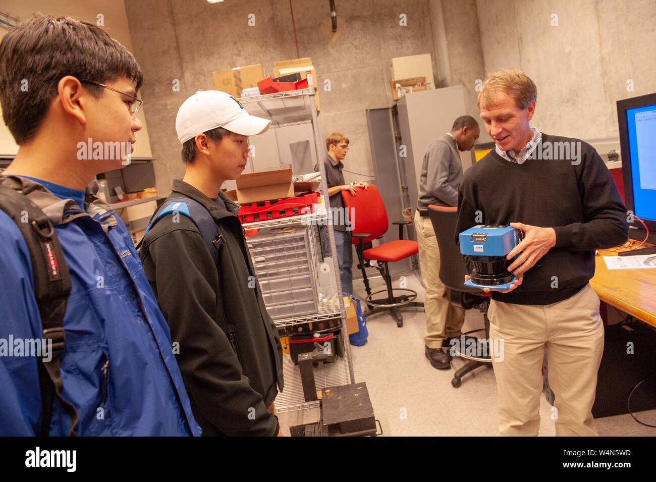 A person shows an apparatus to members of the Johns Hopkins Robotics Club, in a room with computer equipment, at the Johns Hopkins University, Baltimore, Maryland, December, 2009. From the Homewood Photography Collection. () Stock Photo