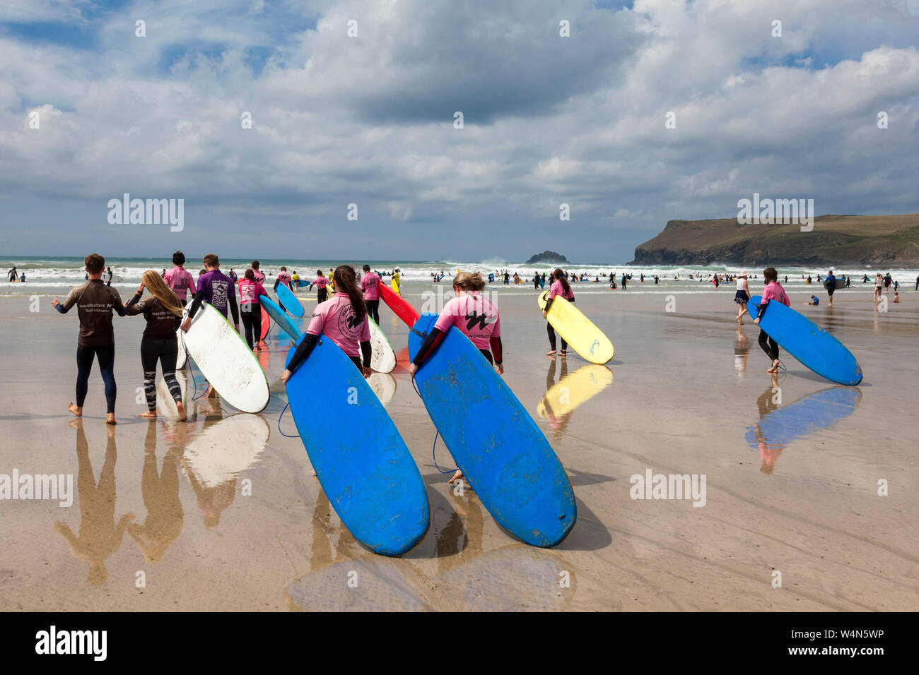 Polzeath, Cornwall, UK. 24th July 2019.  Surfers head to the waves on a hot and sunny afternoon on Polzeath Beach on North Cornwall's Atlantic coast. Stock Photo
