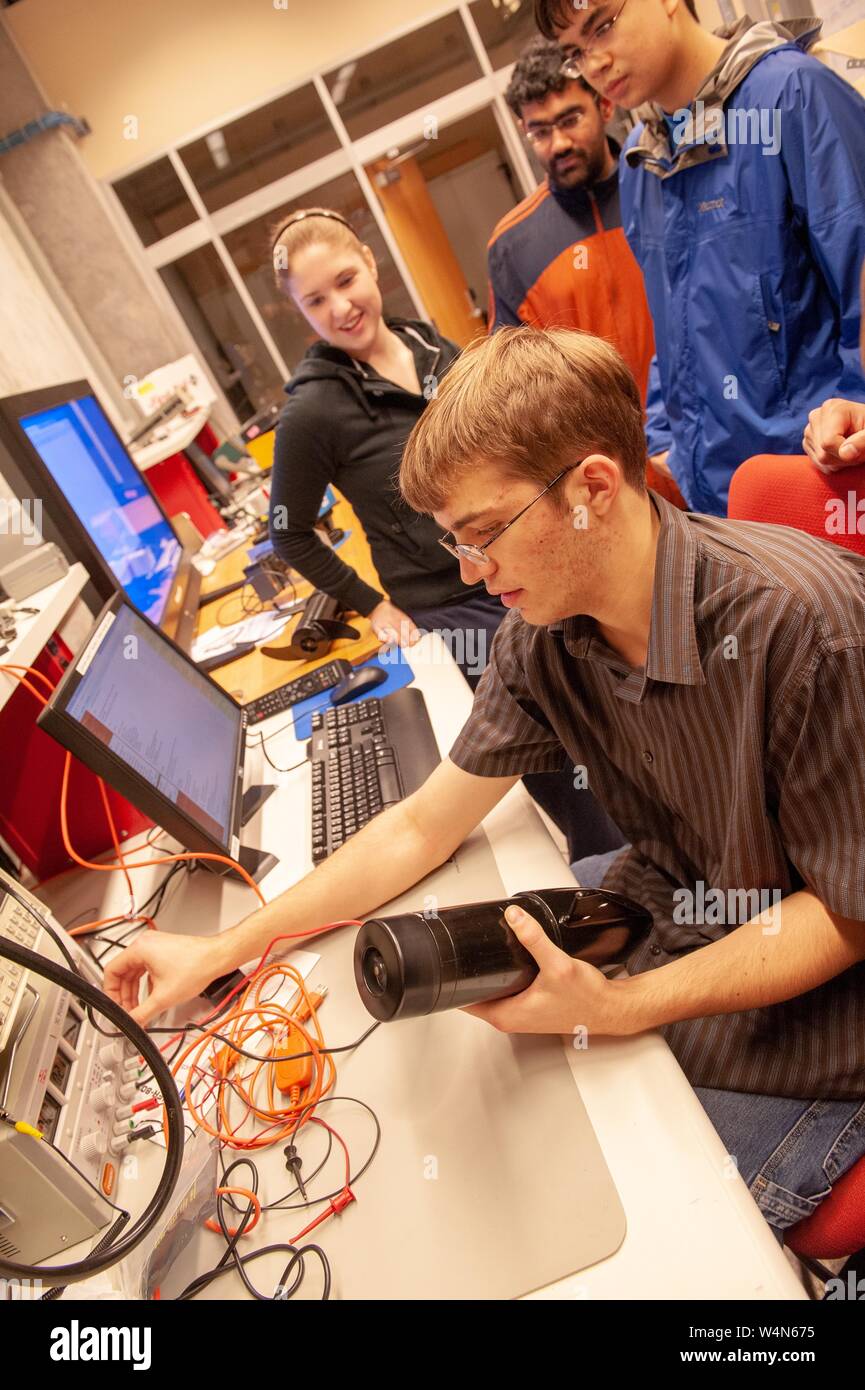 Angled shot of a member of the Johns Hopkins Robotics Club, adjusting a component while colleagues watch, at the Johns Hopkins University, Baltimore, Maryland, December, 2009. From the Homewood Photography Collection. () Stock Photo