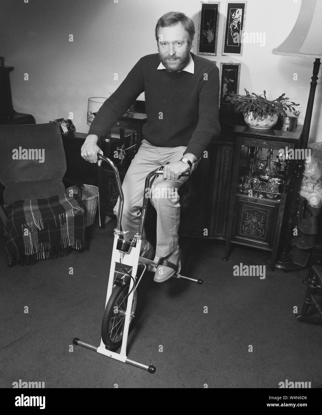 1980s, historical, a man getting some exercise in his front room on a stationary home pedal cycle or mini exercise bike, England, UK. Stock Photo