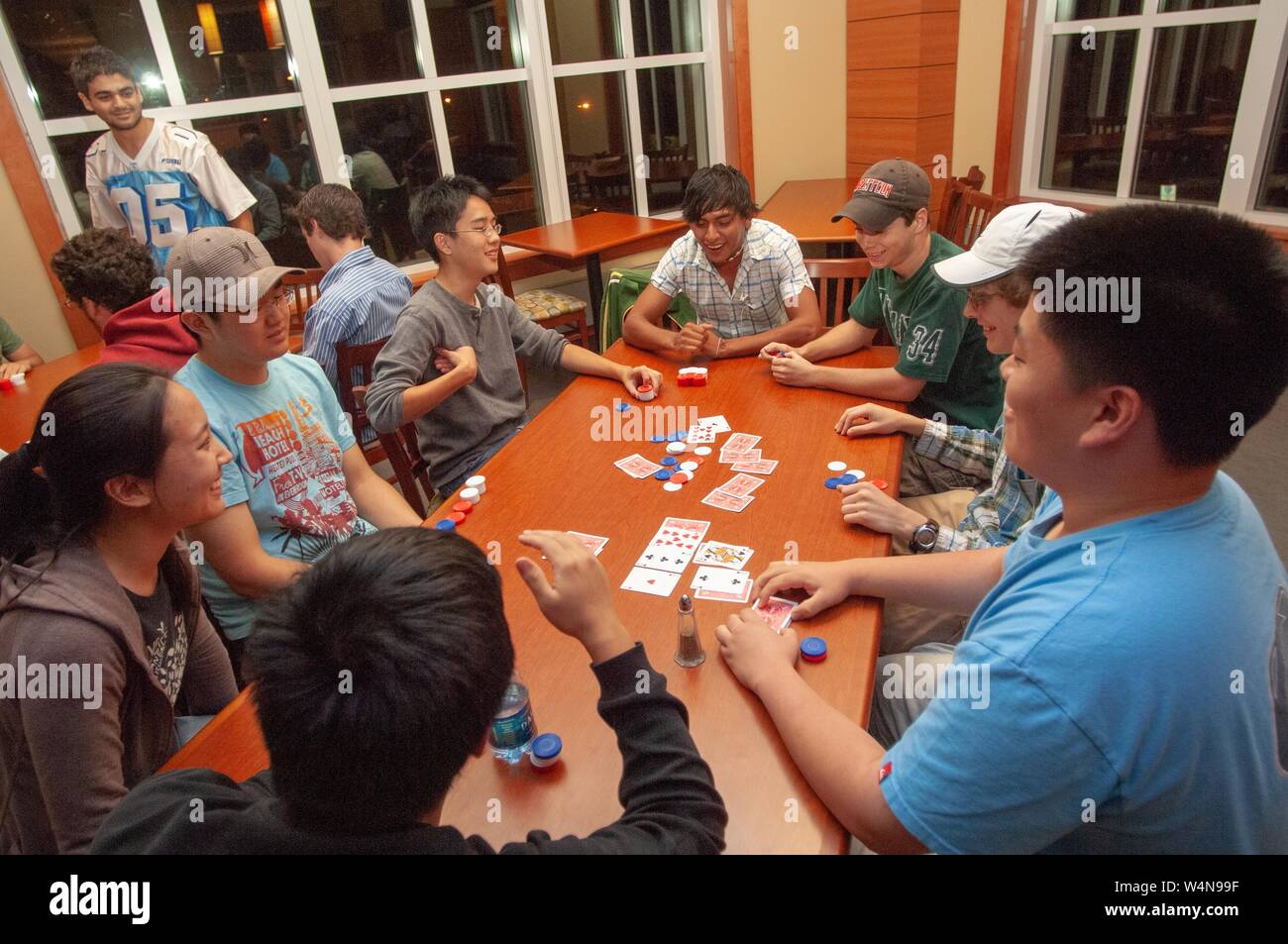 High-angle shot of a group of students, seated around a long wooden table and playing poker, at the Johns Hopkins University, Baltimore, Maryland, September 21, 2006. From the Homewood Photography Collection. () Stock Photo