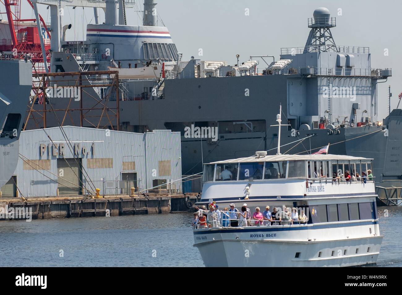 Bow and port view of the Royal Blue, a tourist boat, cruising past Pier No 1 with a large military ship in the background, Baltimore, Maryland, May 4, 2006. From the Homewood Photography Collection. () Stock Photo