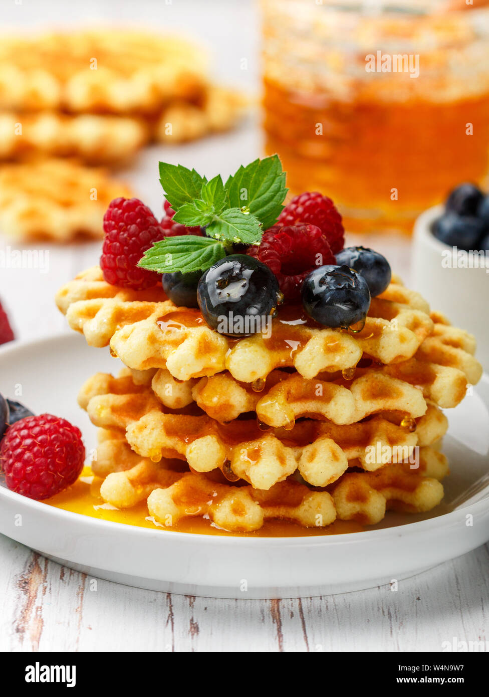 Viennese crispy waffles with fresh berries (raspberries and blueberries) with honey and mint leaves on a white plate on the table. Delicious homemade Stock Photo