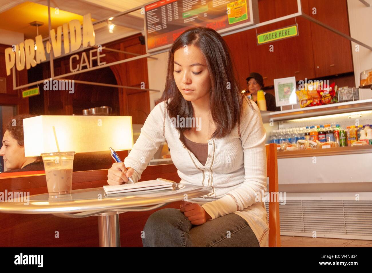 Student sitting at a table in a Pura Vida Cafe and writing notes in a ring binder, at the Johns Hopkins University, Baltimore, Maryland, October 12, 2007. From the Homewood Photography Collection. () Stock Photo