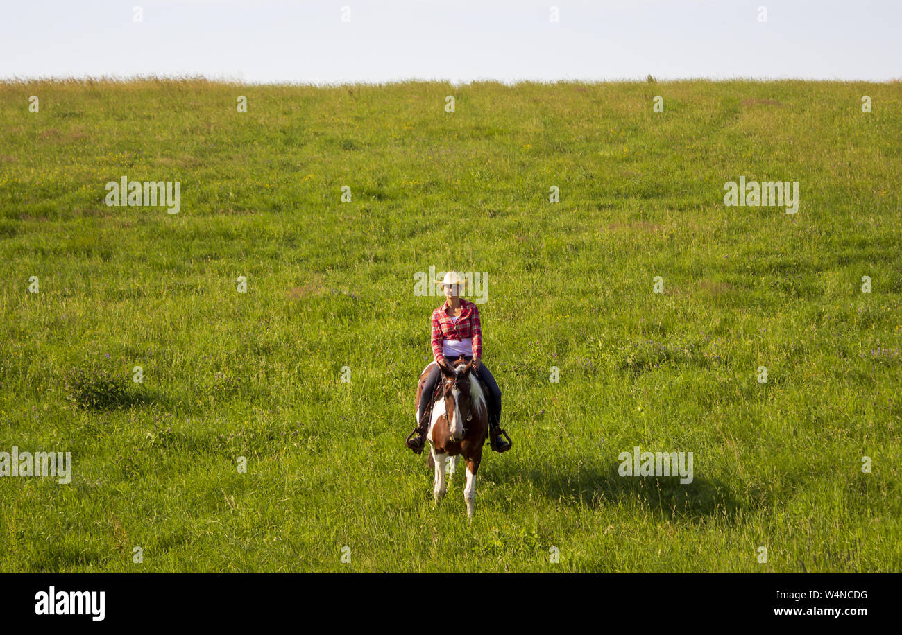 A young girl rides a horse on a pasture near a ranch Stock Photo