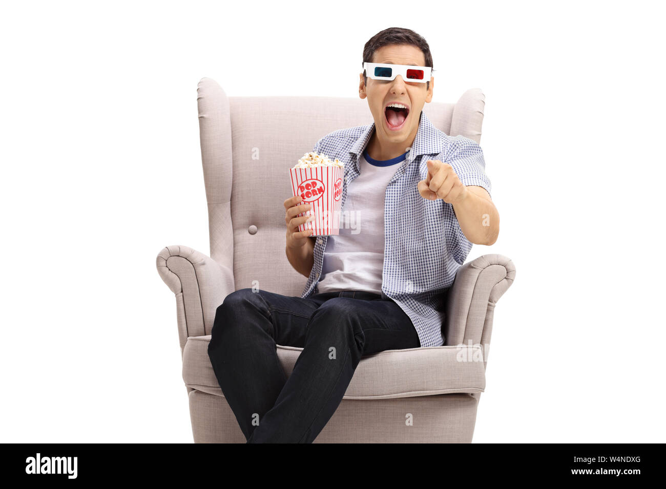 Guy with 3D glasses and popcorn in an armchair laughing and pointing at the camera isolated on white background Stock Photo