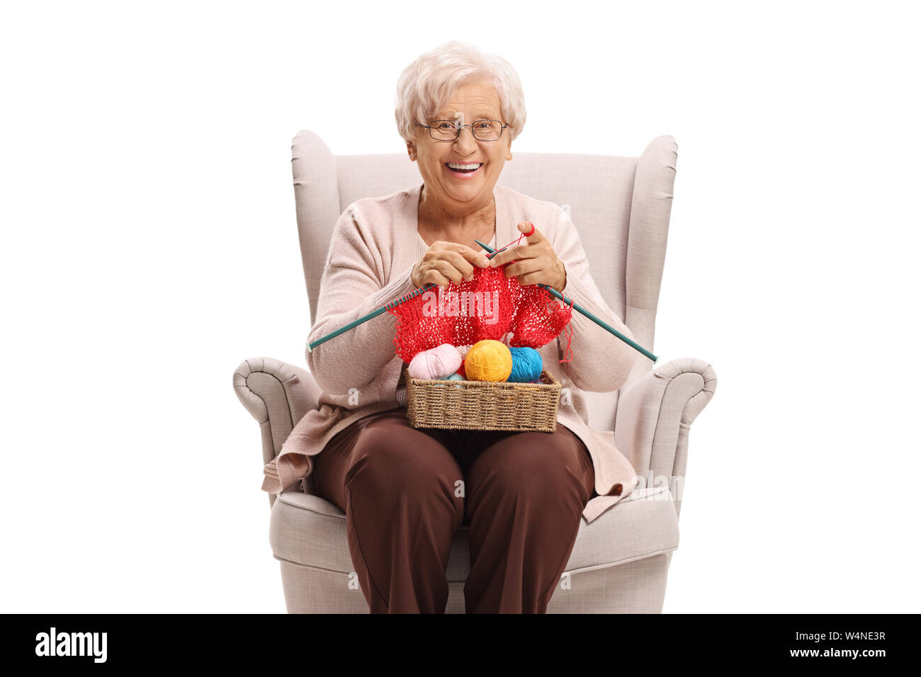 Elderly woman in an armchair knitting and smiling at the camera ...