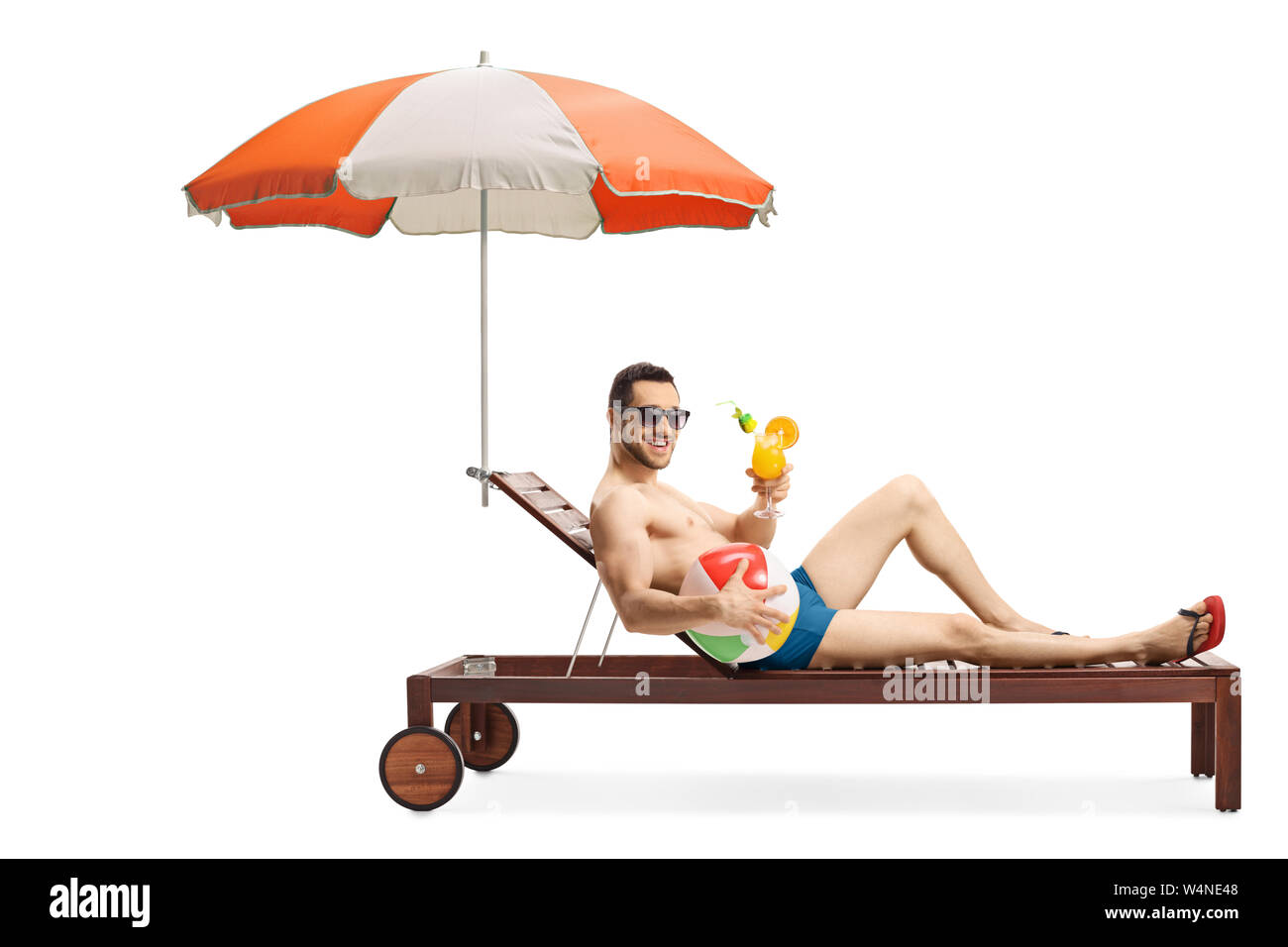 Full length shot of a young man on a sunbed with an umbrella holding an inflatable ball and a cocktail isolated on white background Stock Photo