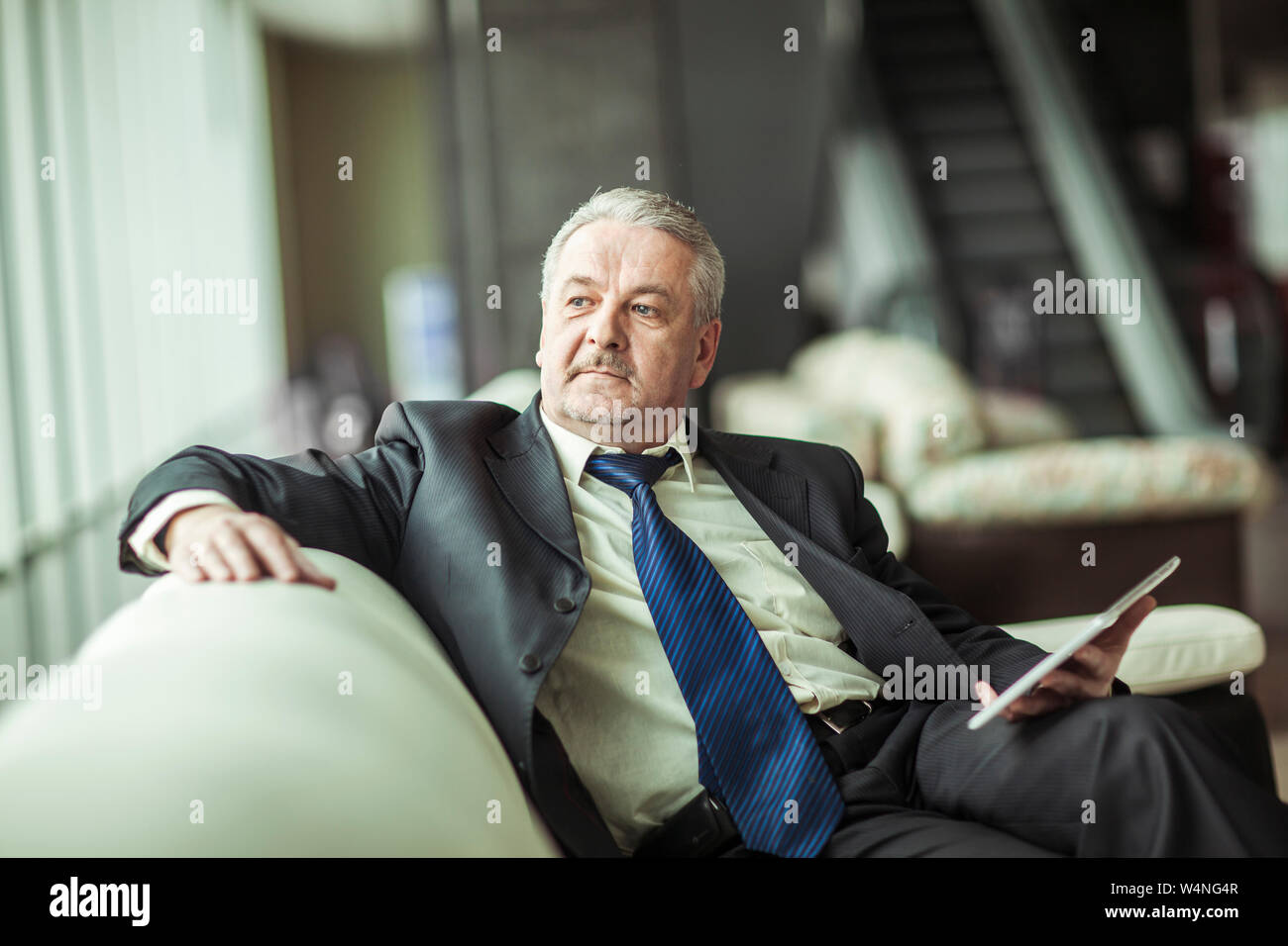 experienced businessman with digital tablet sitting on the sofa in the private office. Stock Photo