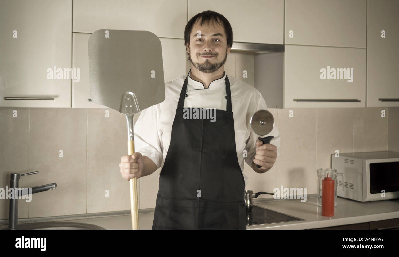 Attractive young funny man dancing while cooking in the kitchen at home ...