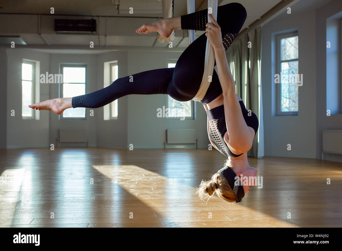 Beautiful girl aerial yoga trainer shows medutiruet on hanging lines
