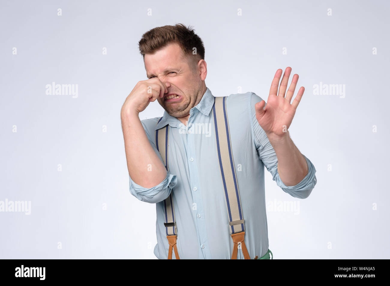 Displeased young man plugs nose as smells something stink and unpleasant. Stock Photo