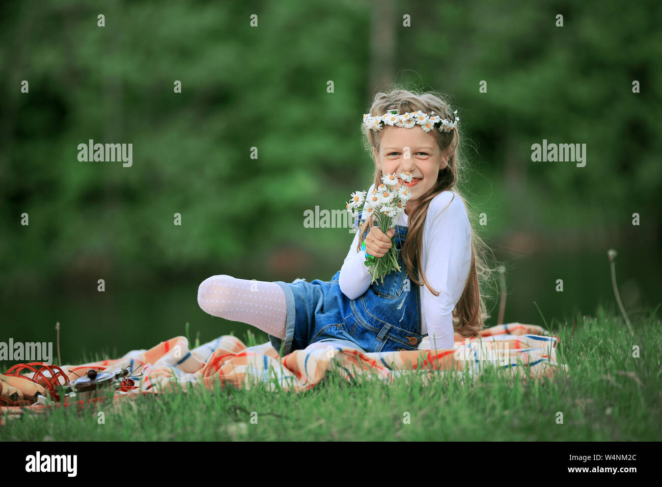 cute little girl in a wreath and a bouquet of wildflowers on a picnic ...