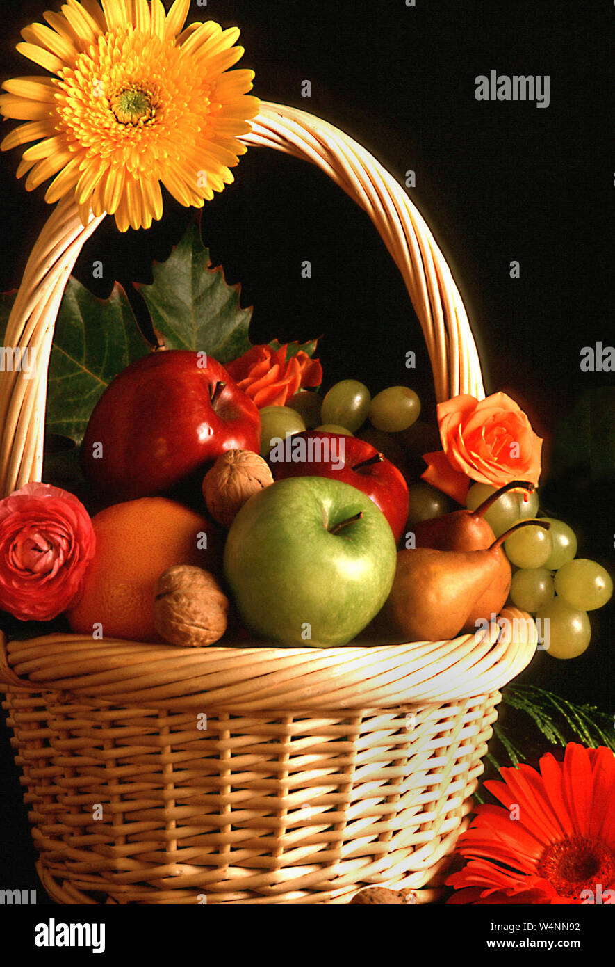 Still life of wicker basket with different fruits and flowers on black ...